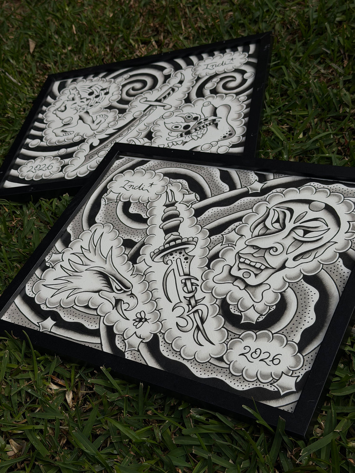 Angled view of two framed Indi Giblin flash sheets, showing the eagle, dagger and mask composition in the foreground.